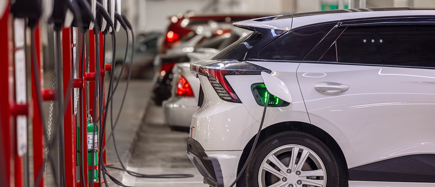 A row of passenger EVs being charged in a car park. A row of passenger EVs being charged in a car park.