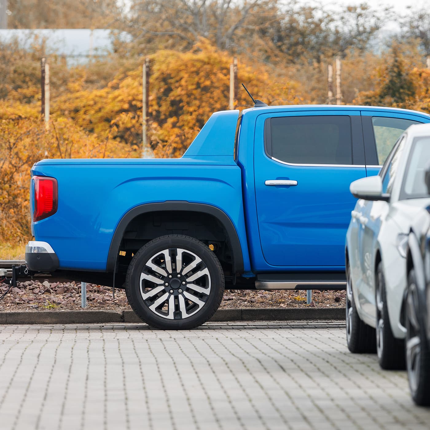 Side view of new blue EV pickup truck parked at outdoor parking lot automobile dealer or parking place against autumn foliage. Side view of new blue EV pickup truck parked at outdoor parking lot automobile dealer or parking place against autumn foliage.