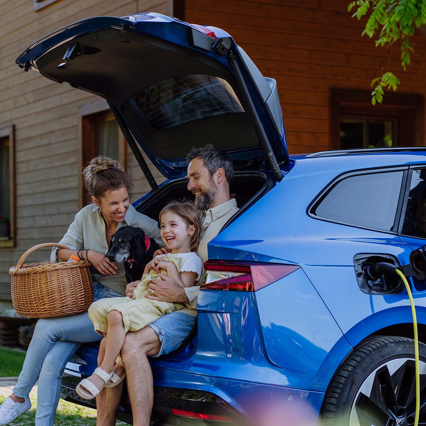 A happy family sitting in the trunk of their EV while its plugged in to a charger. A happy family sitting in the trunk of their EV while its plugged in to a charger.